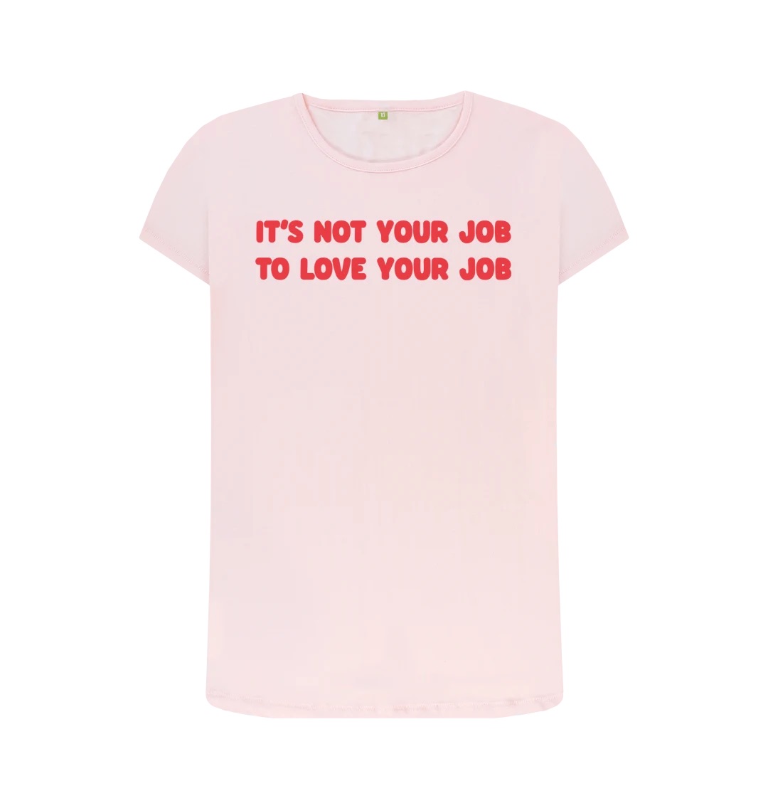 A light pink t-shirt with a large dark pink text along the front on two lines reading It's Not Your Job To Love Your Job.